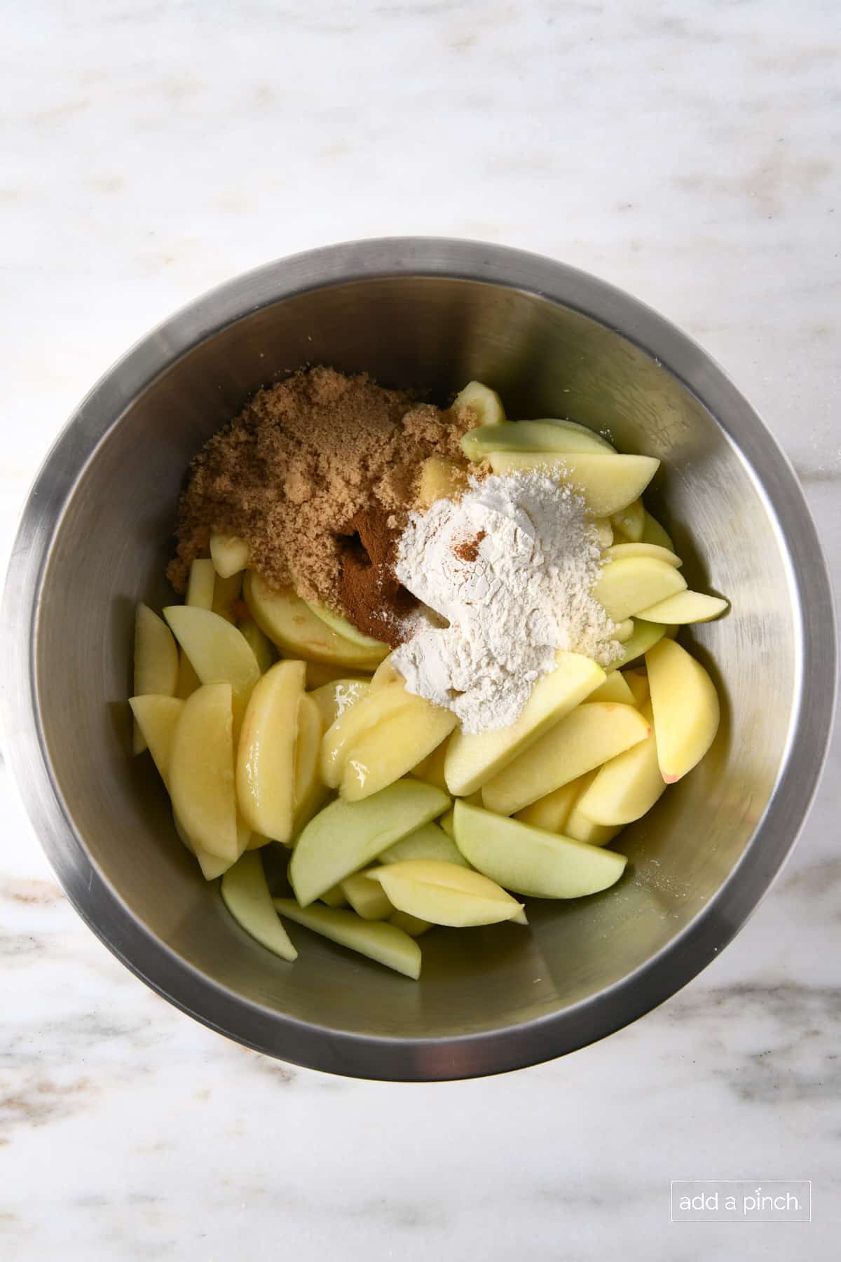 Apple filling ingredients - slices apples, brown sugar, flour, baking powder, cinnamon, salt and lemon juice in stainless mixing bowl.