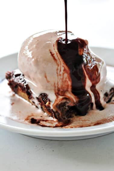 Chocolate chip cookie brownie on a white plate with chocolate syrup drizzled over the top.