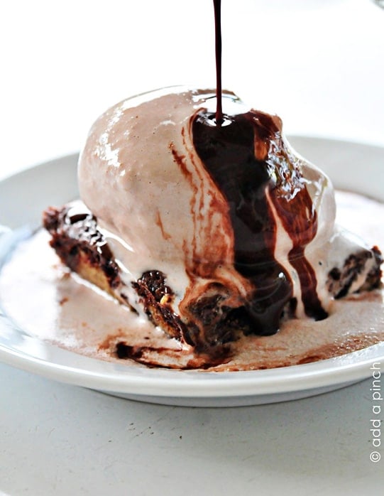 Closeup photo of chocolate chip cookie brownie topped with chocolate ice cream with chocolate syrup being drizzled on top.