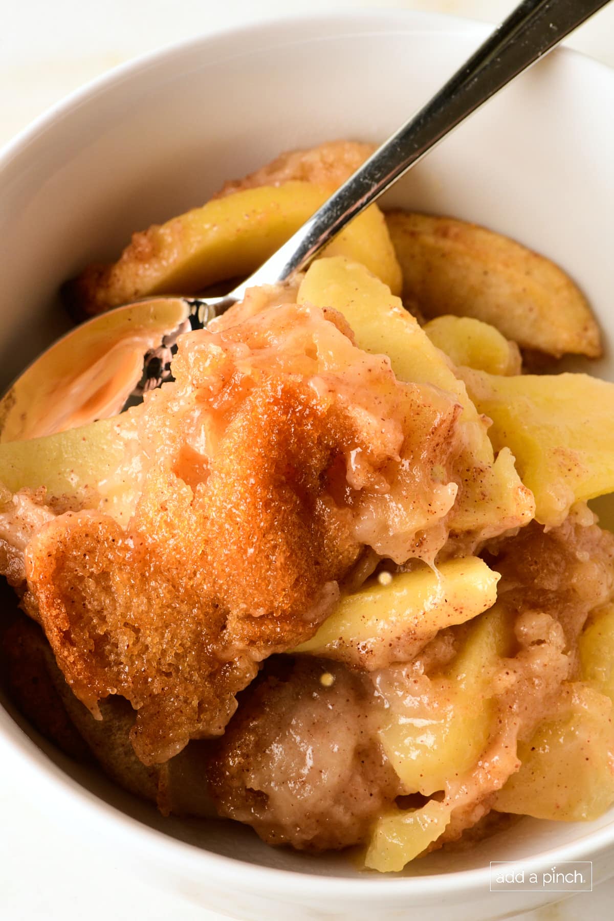 Apple cobbler in a white bowl with a spoon.