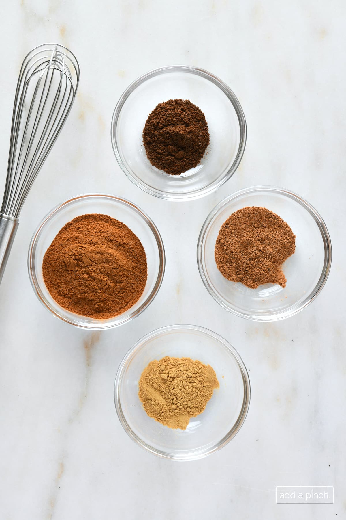 Glass bowls with cinnamon, allspice, nutmeg and ginger along with a whisk.