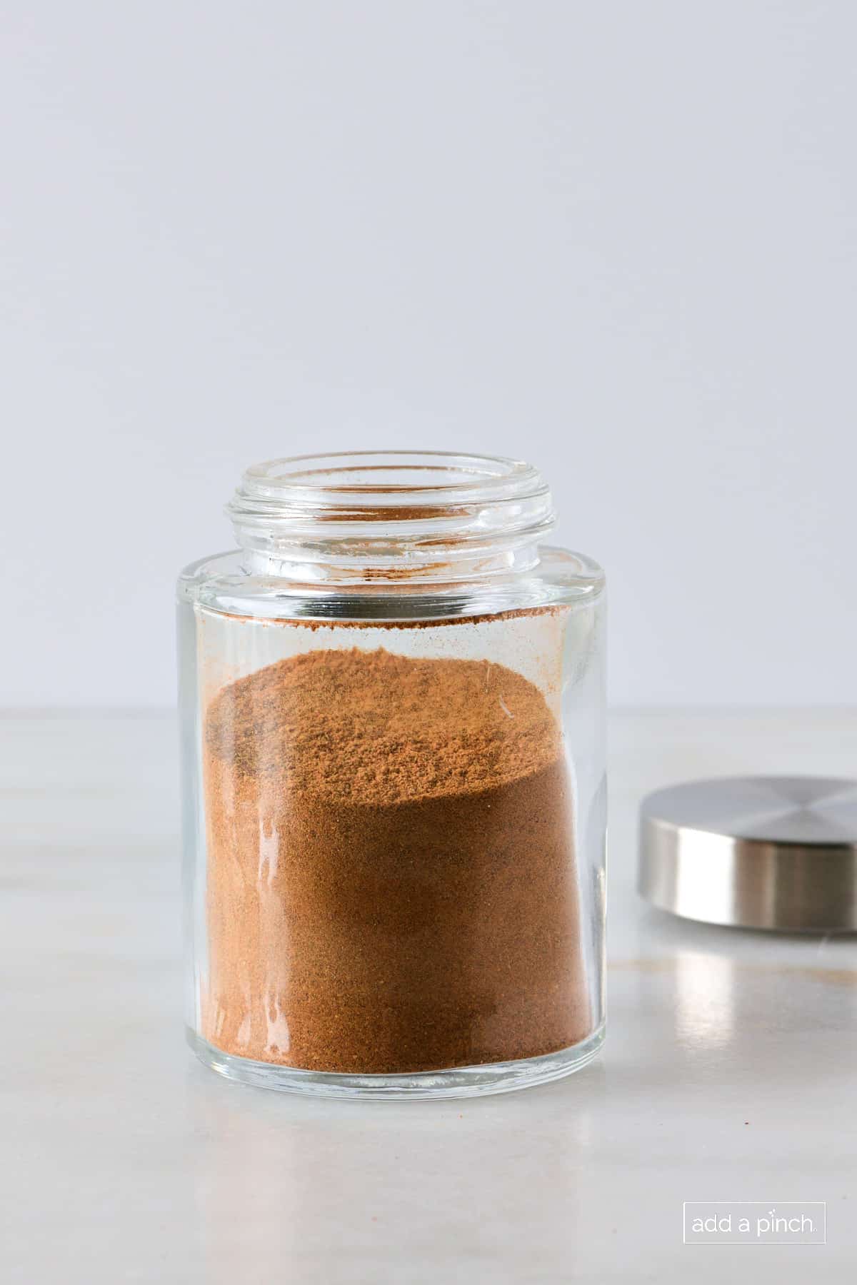 Glass container with metal airtight lid filled with apple pie spice.