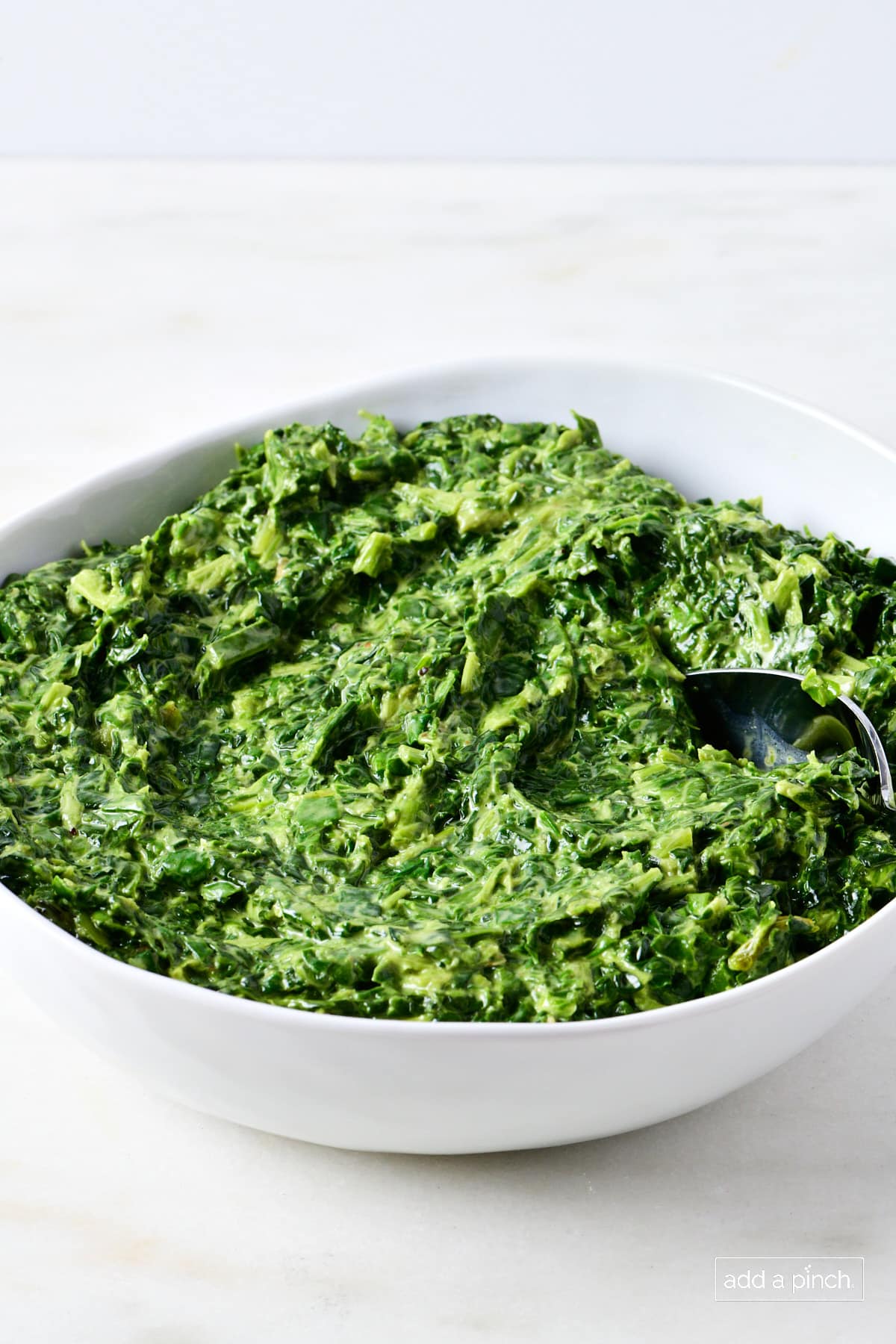 Creamed spinach in a white serving bowl with a spoon.