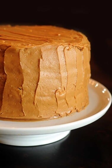 Caramel cake on a white cake stand on a dark wooden table.