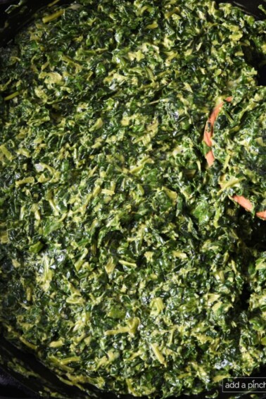 Creamed spinach in a skillet with a wooden spoon.