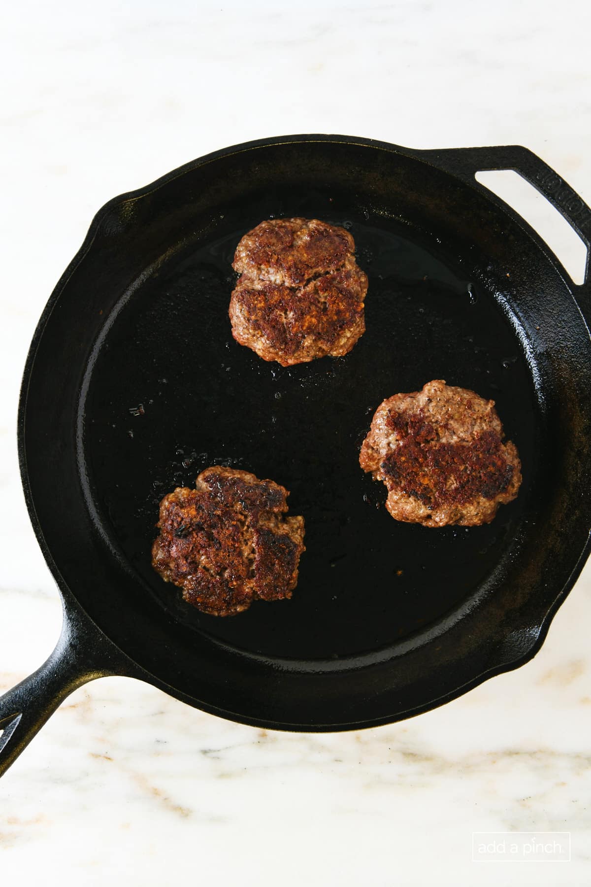Cooked hamburger patties in a cast iron skillet.