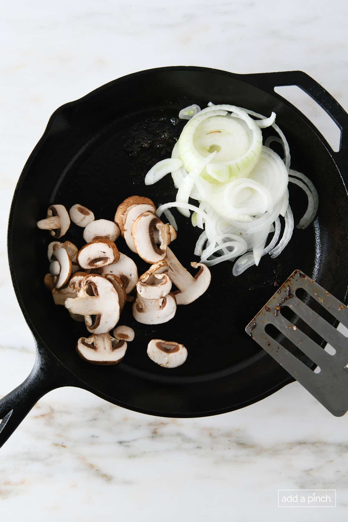 Mushroom and onions in a skillet with a metal spatula.