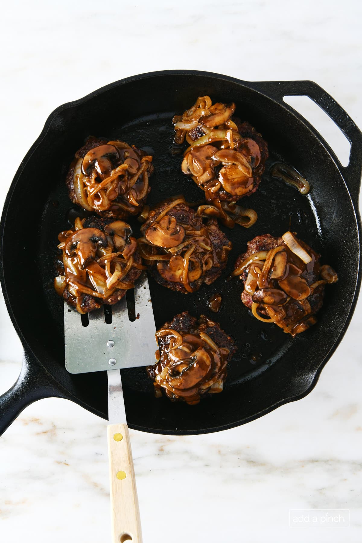 Hamburger steak topped with mushroom and onion gravy in skillet with spatula for serving.