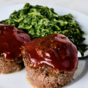 Two meatloaf muffins on a white plate with creamed spinach.