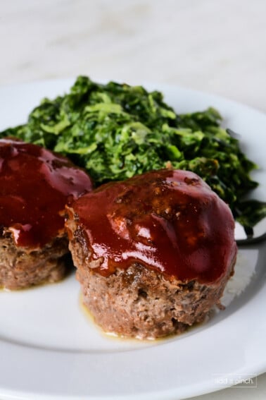 Two meatloaf muffins on a white plate with creamed spinach.