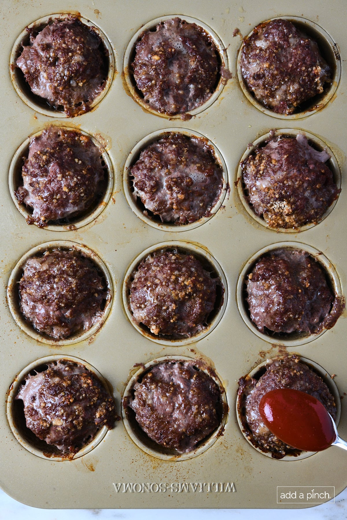 Baked meatloaf muffins in a muffin pan with bbq glaze being spooned onto them.