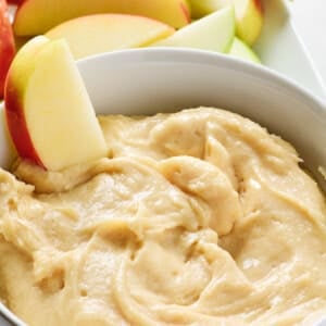 Sliced apples surround and are dipped into a bowl of creamy apple dip.
