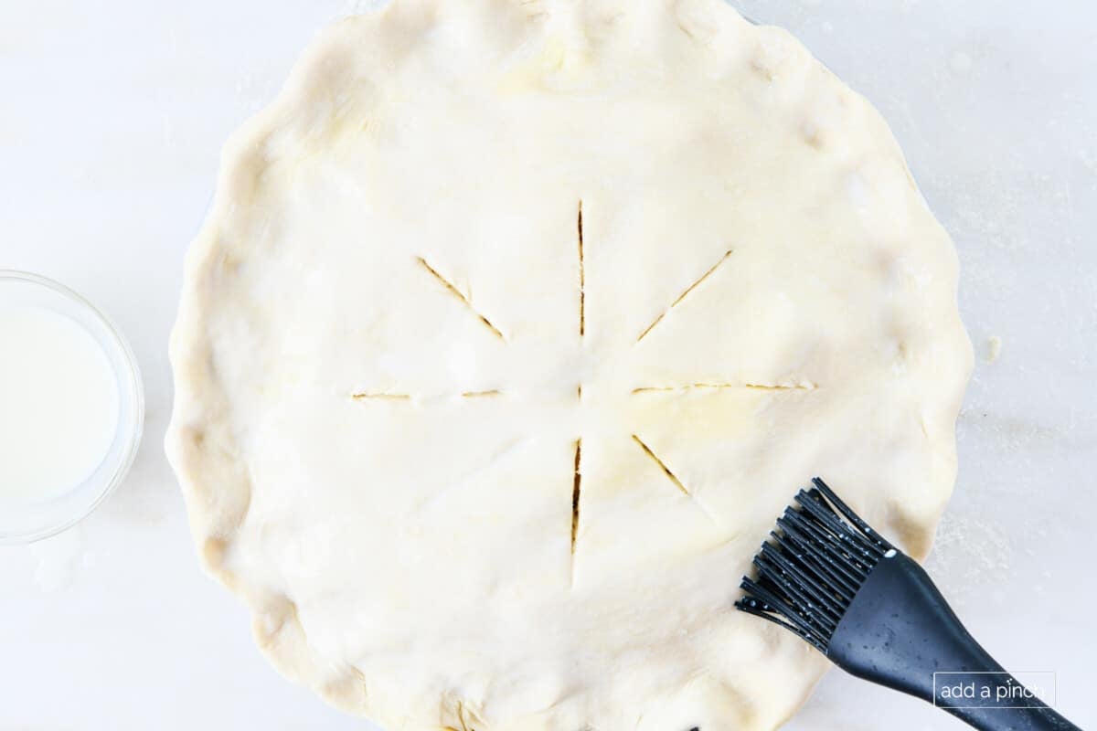 Brushing milk on top pie dough with a black brush.