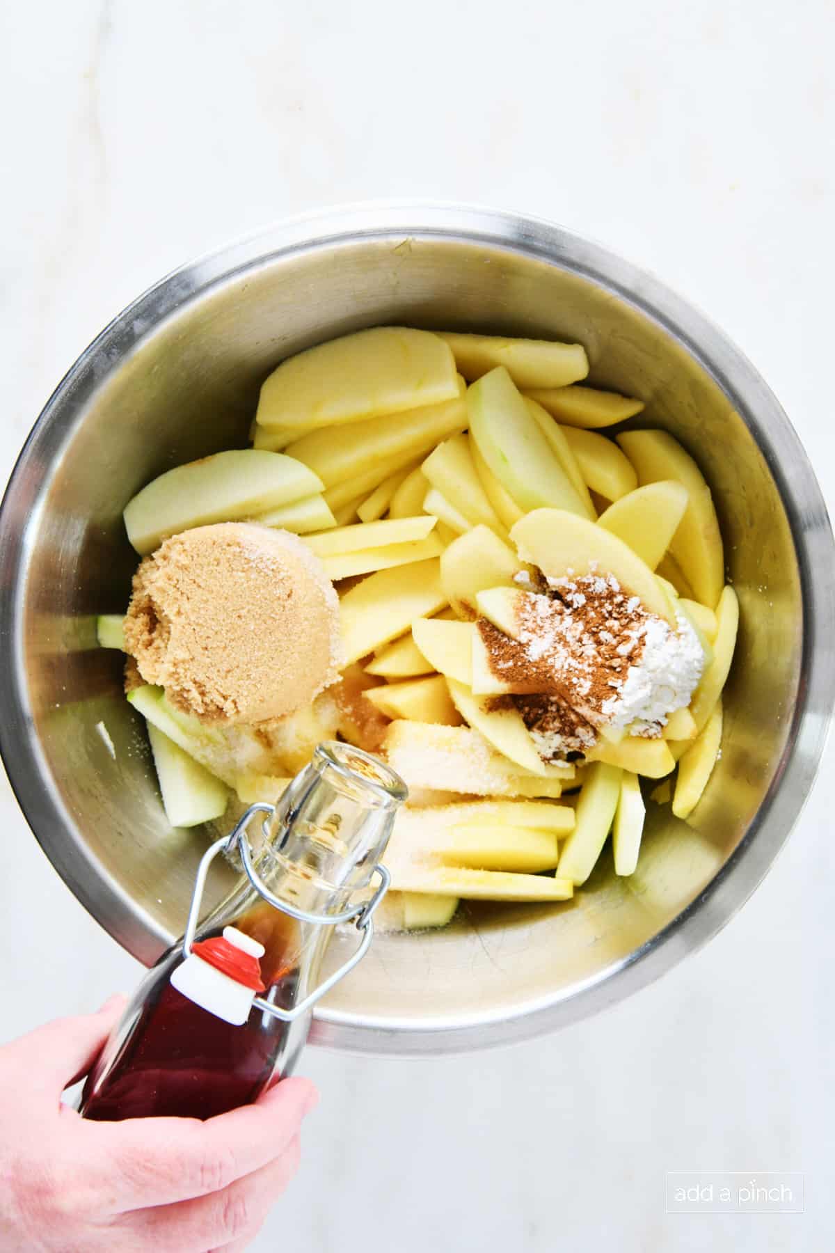 Adding vanilla extract to the apple pie filling ingredients in a mixing bowl.