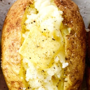 Baked potato with butter, salt and pepper on a white platter.