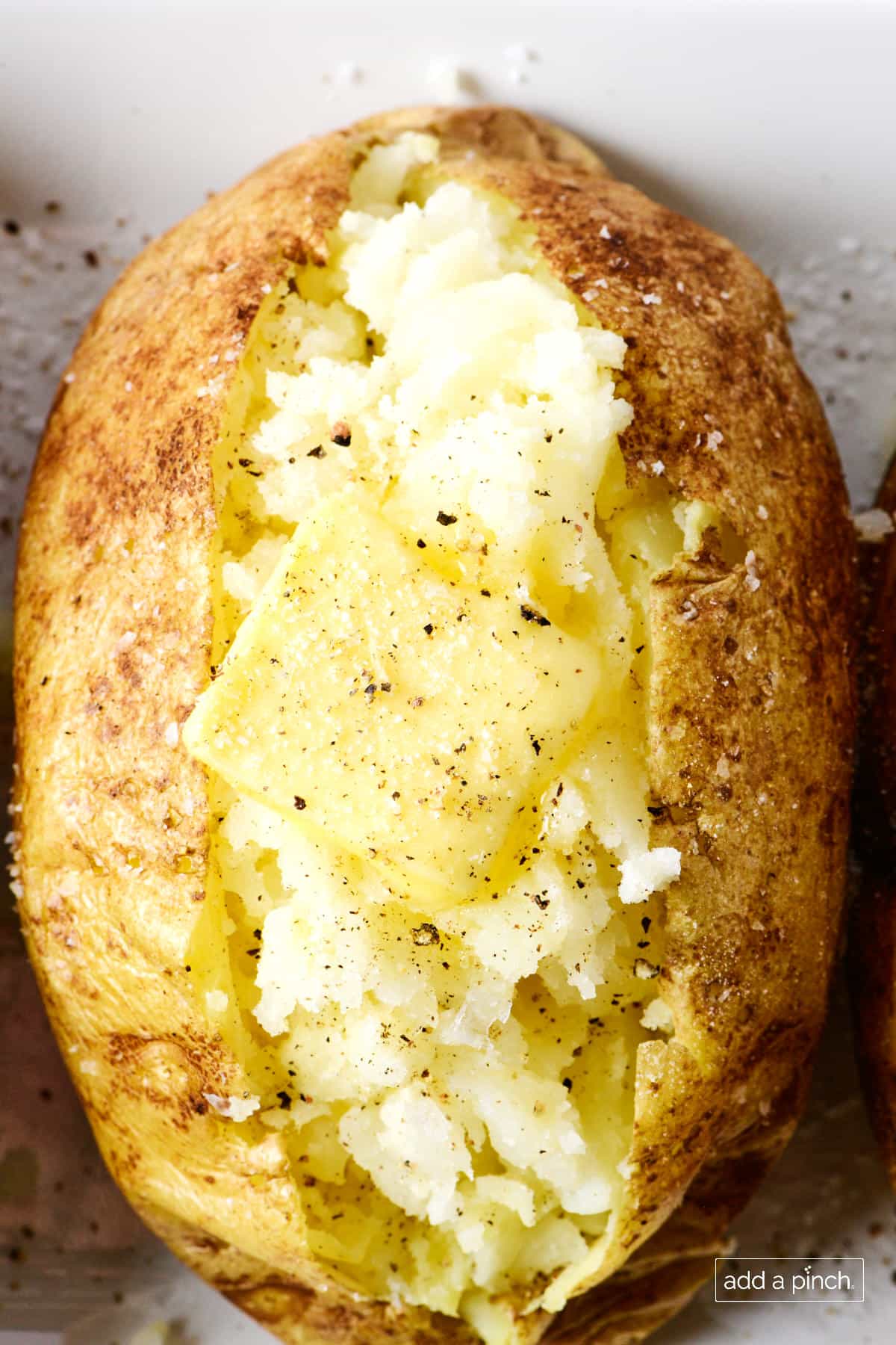 Baked potato with butter, salt and pepper on a white platter.