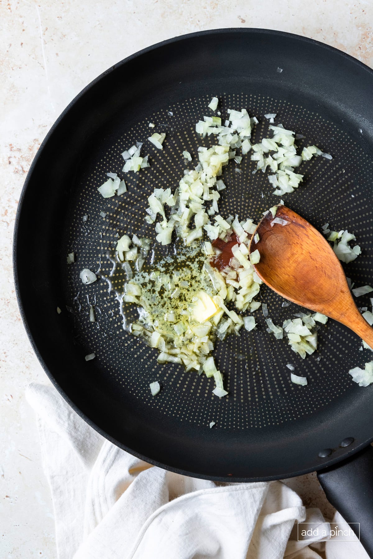 Garlic and onions sauteeing in a skillet with a wooden spoon.