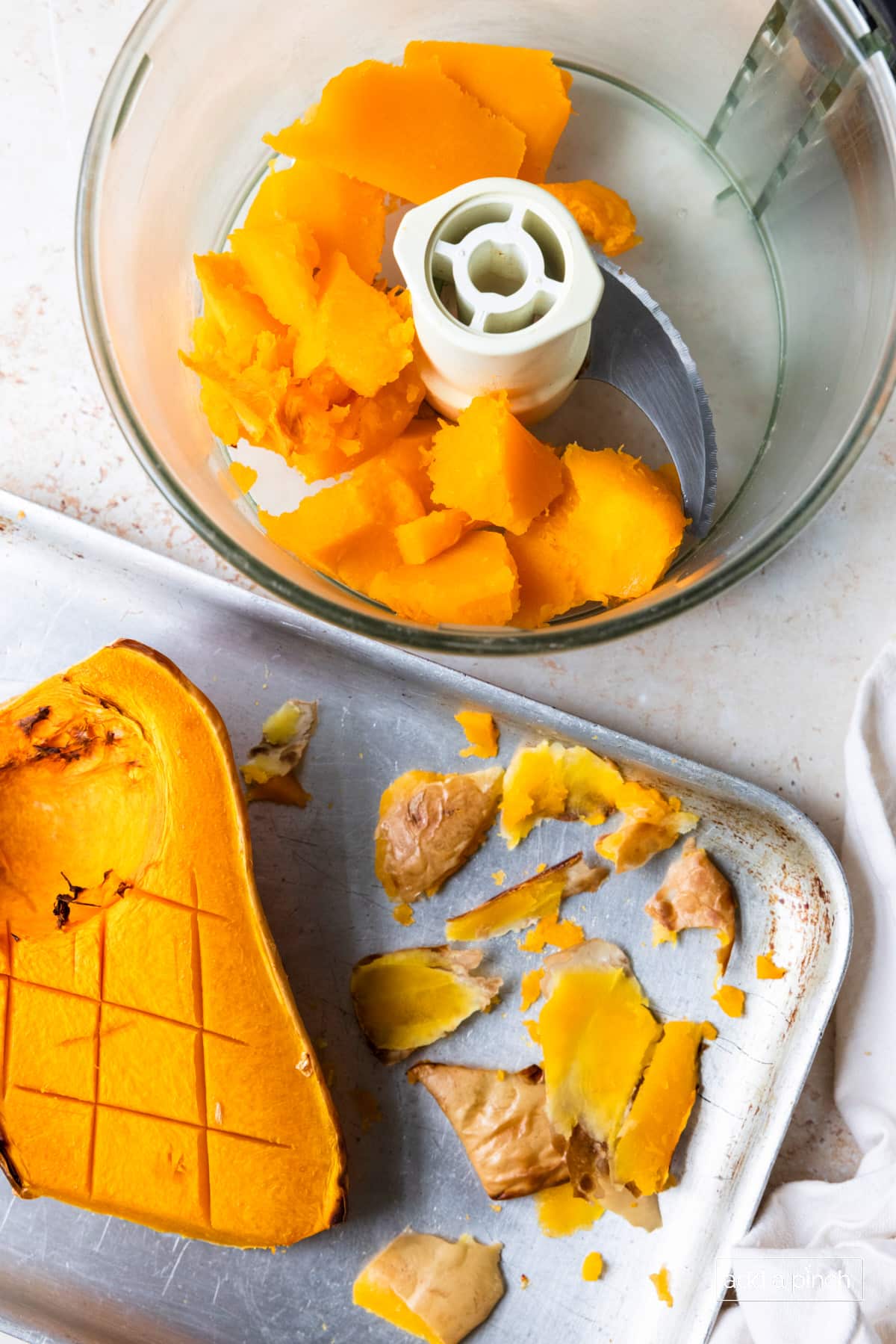 Roasted butternut squash on a baking sheet and being added to a food processor.