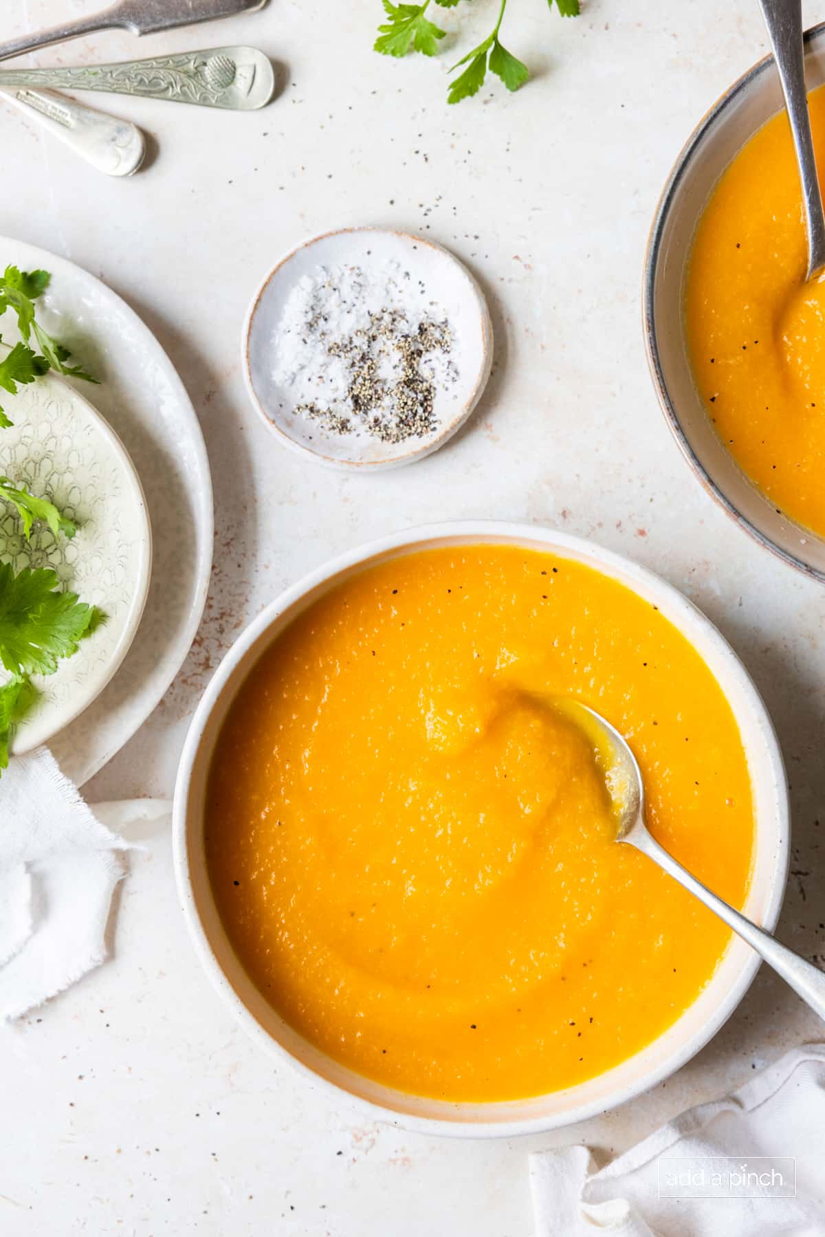 Butternut squash soup in bowls, surrounded by garnishes and salt and pepper.