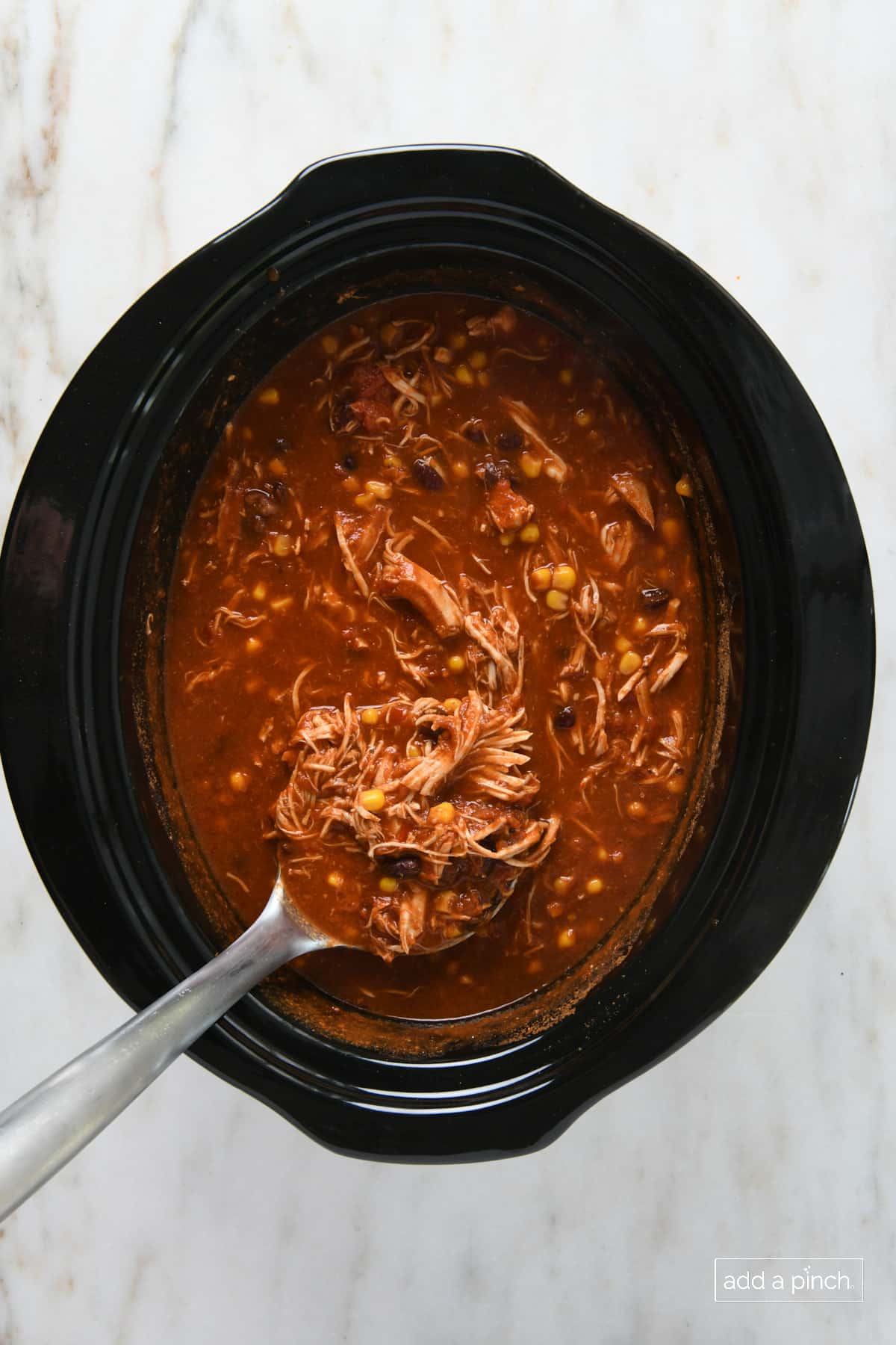 Shredded chicken has been added back to chicken tortilla soup in a slow cooker insert. 