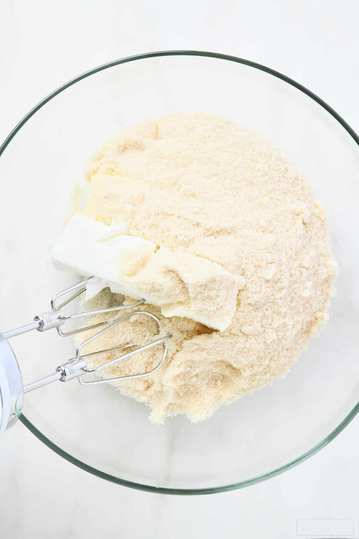 A glass mixing bowl holds softened butter, shortening and sugar being creamed together by a hand mixer.