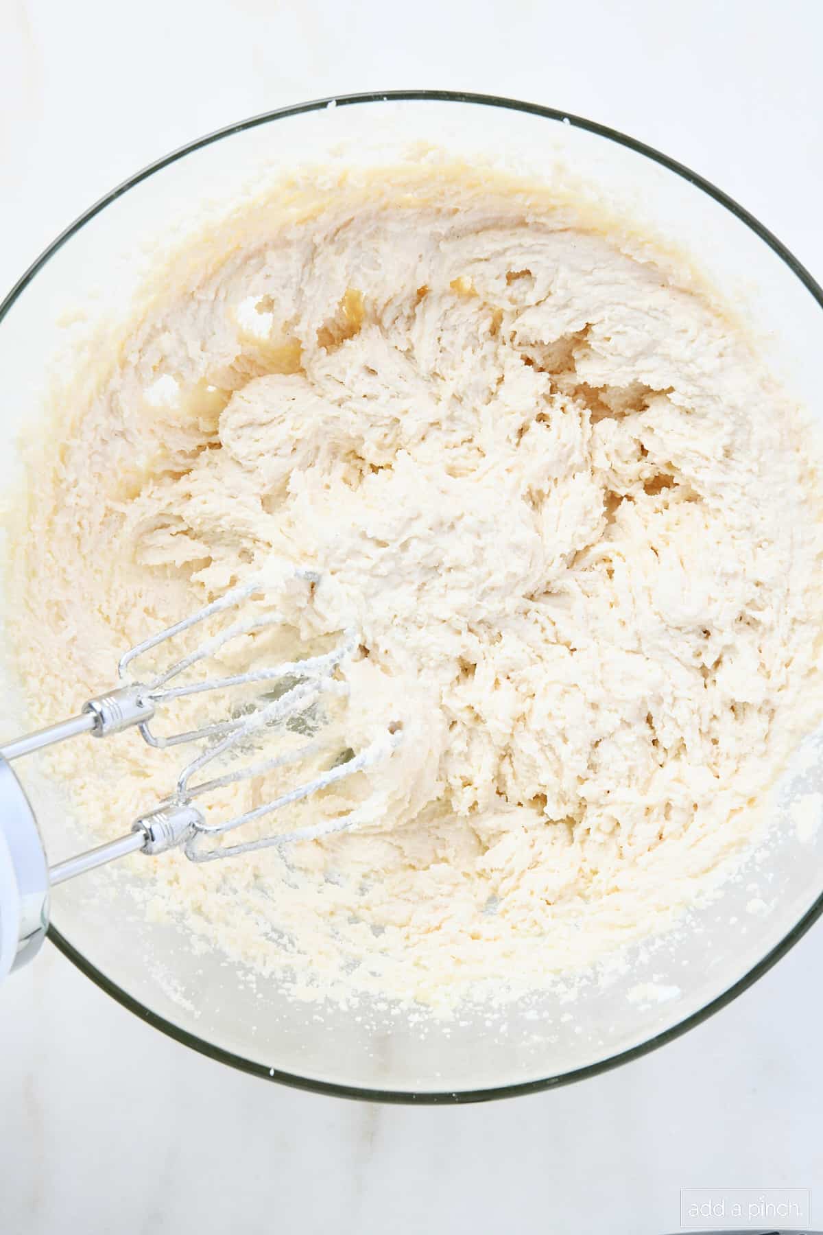 Light and fluffy creamed butter, sugar and shortening in a glass bowl with a. hand mixer inside.