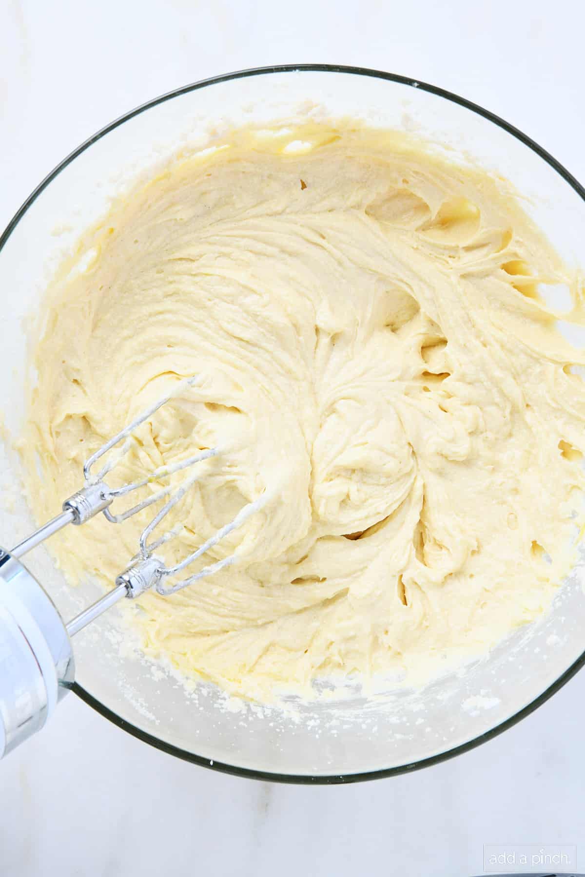 A hand mixer finishes mixing in the last egg into the pound cake batter in a glass mixing bowl.