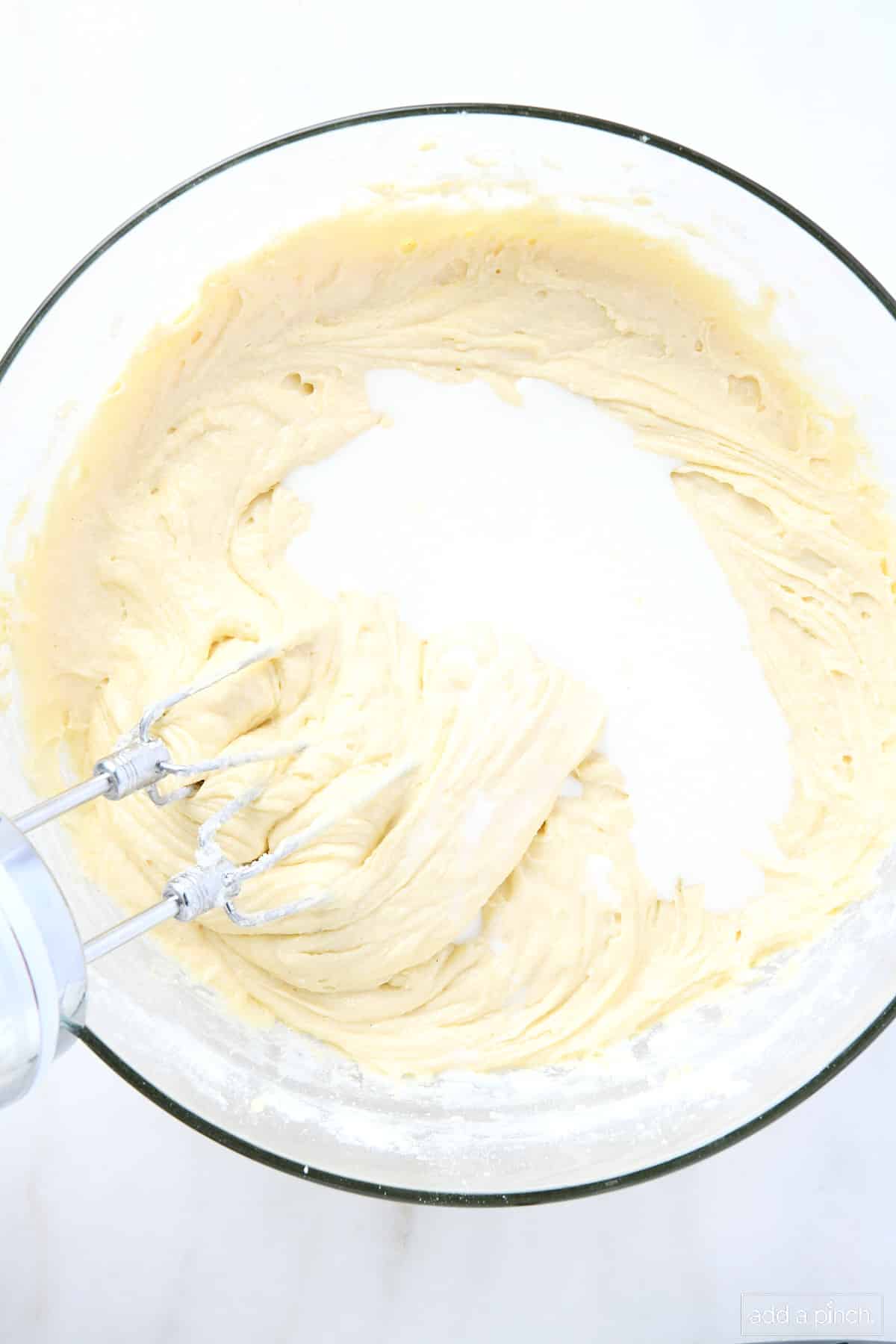 Milk is added to a glass mixing bowl and is being mixed into cake batter with hand mixer.