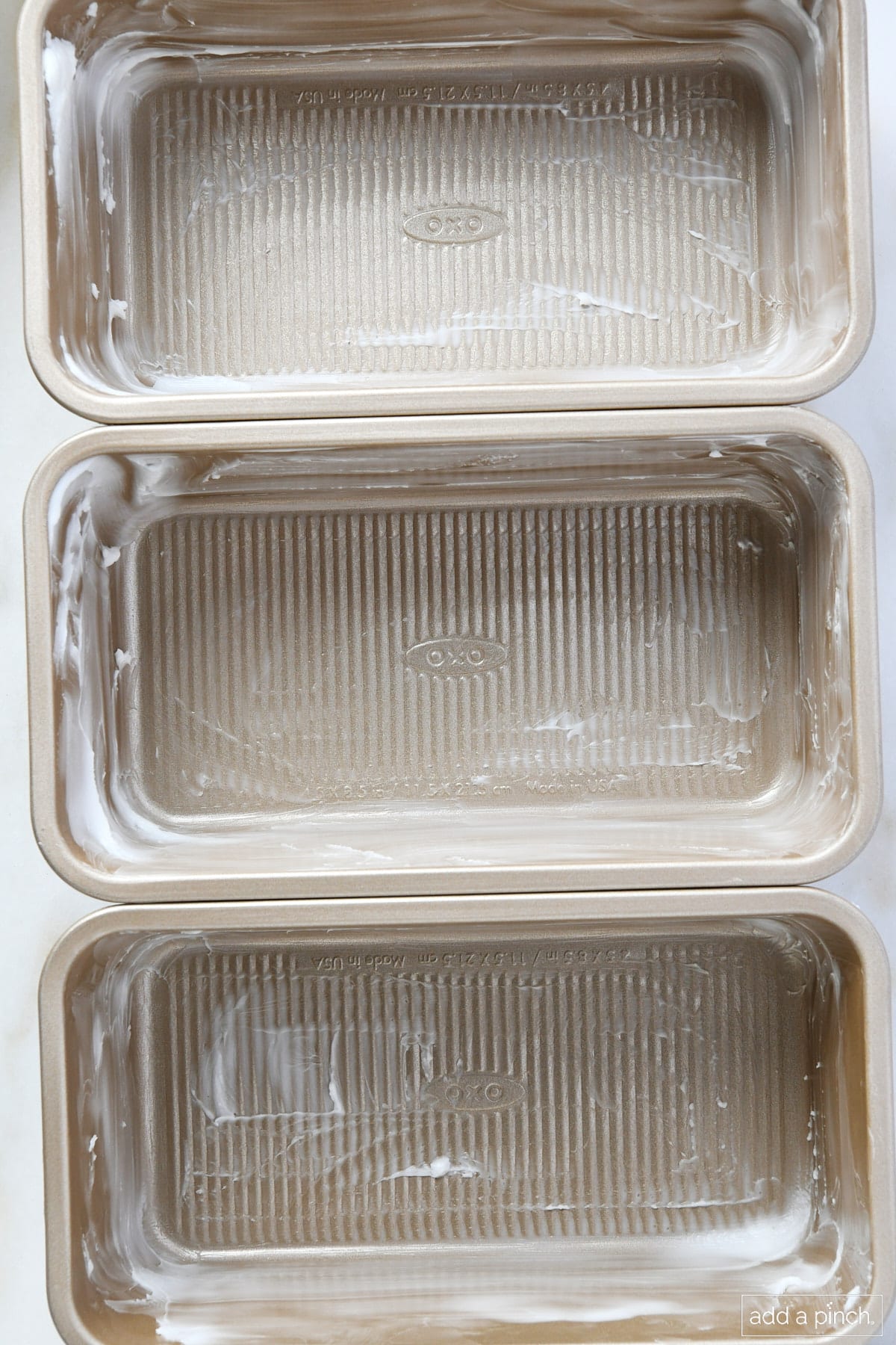 Three loaf pans are rubbed with vegetable shortening to prep them for baking.