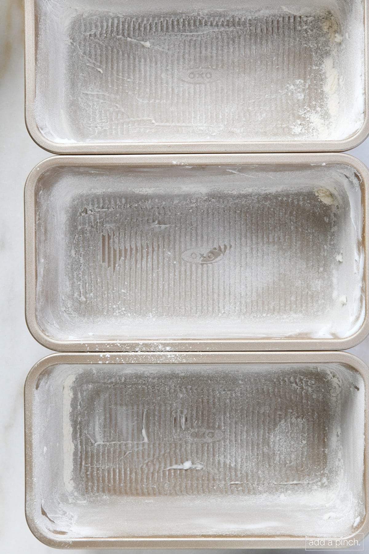 Three loaf pans have been completely  prepped with shortening and dusting with flour and are ready for baking.