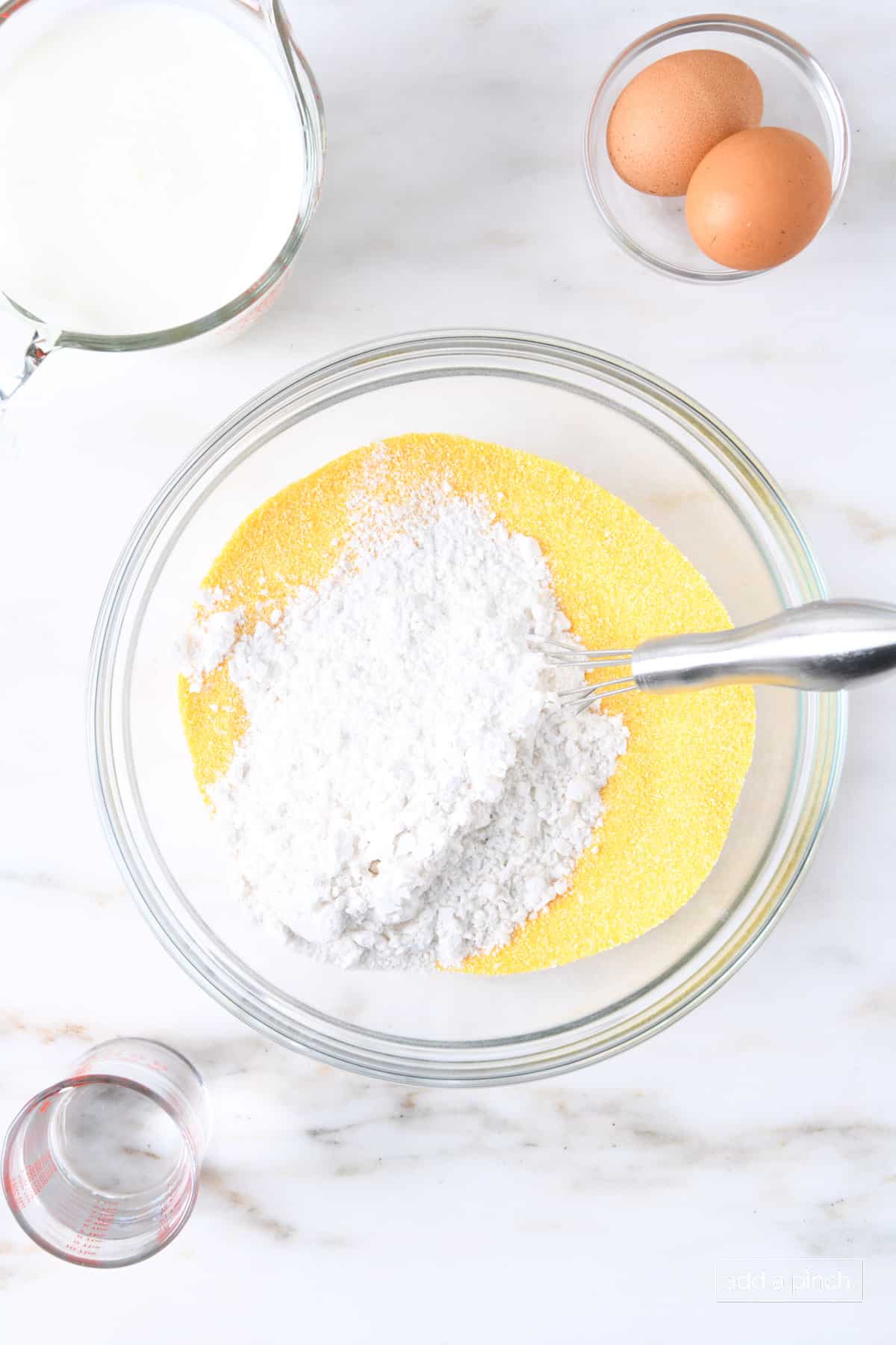 Flour added to cornmeal in a glass bowl.