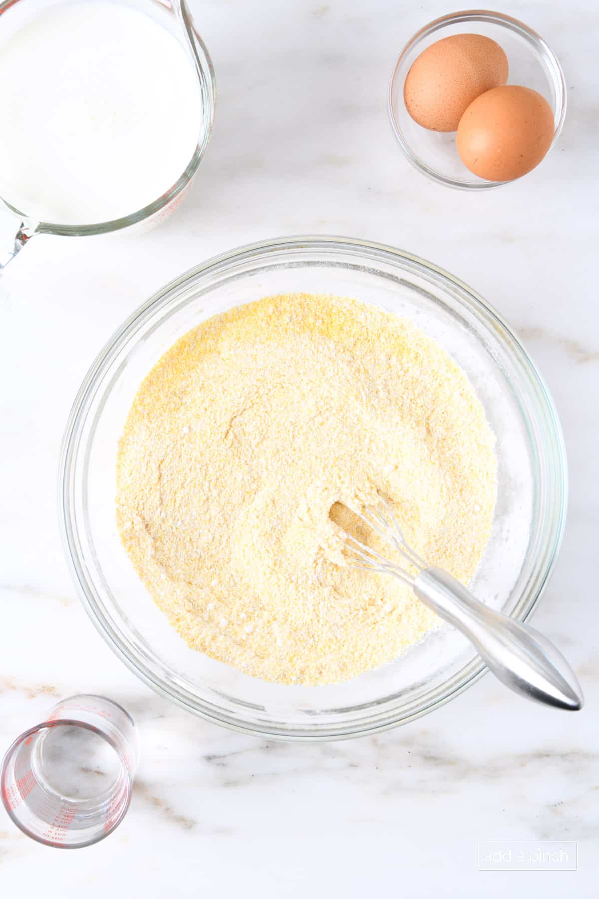 Whisked flour and cornmeal in a glass bowl with a whisk.