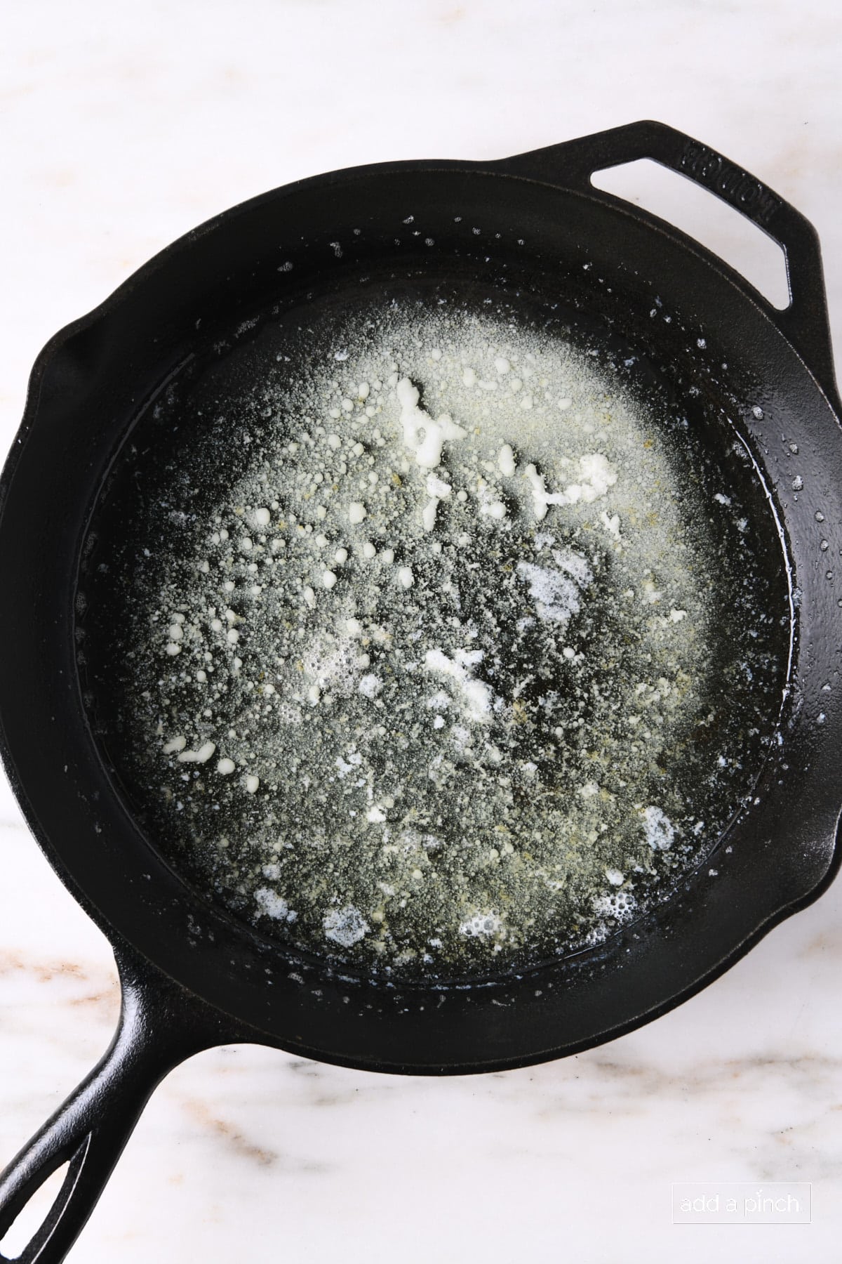 Skillet with melted butter on a marble countertop.
