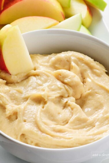 Sliced apples surround and are dipped into a bowl of creamy apple dip.