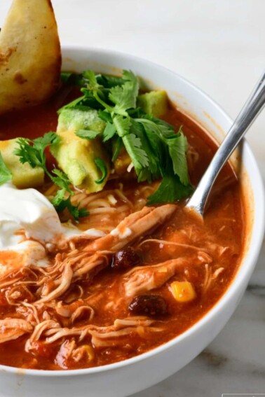 Bowl of chicken tortilla soup garnished with avocados, cilantro, crispy tortilla strips and sour cream.