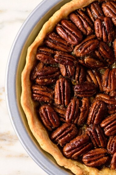 Pecan pie with golden pie crust in a pie plate on a marble counter.