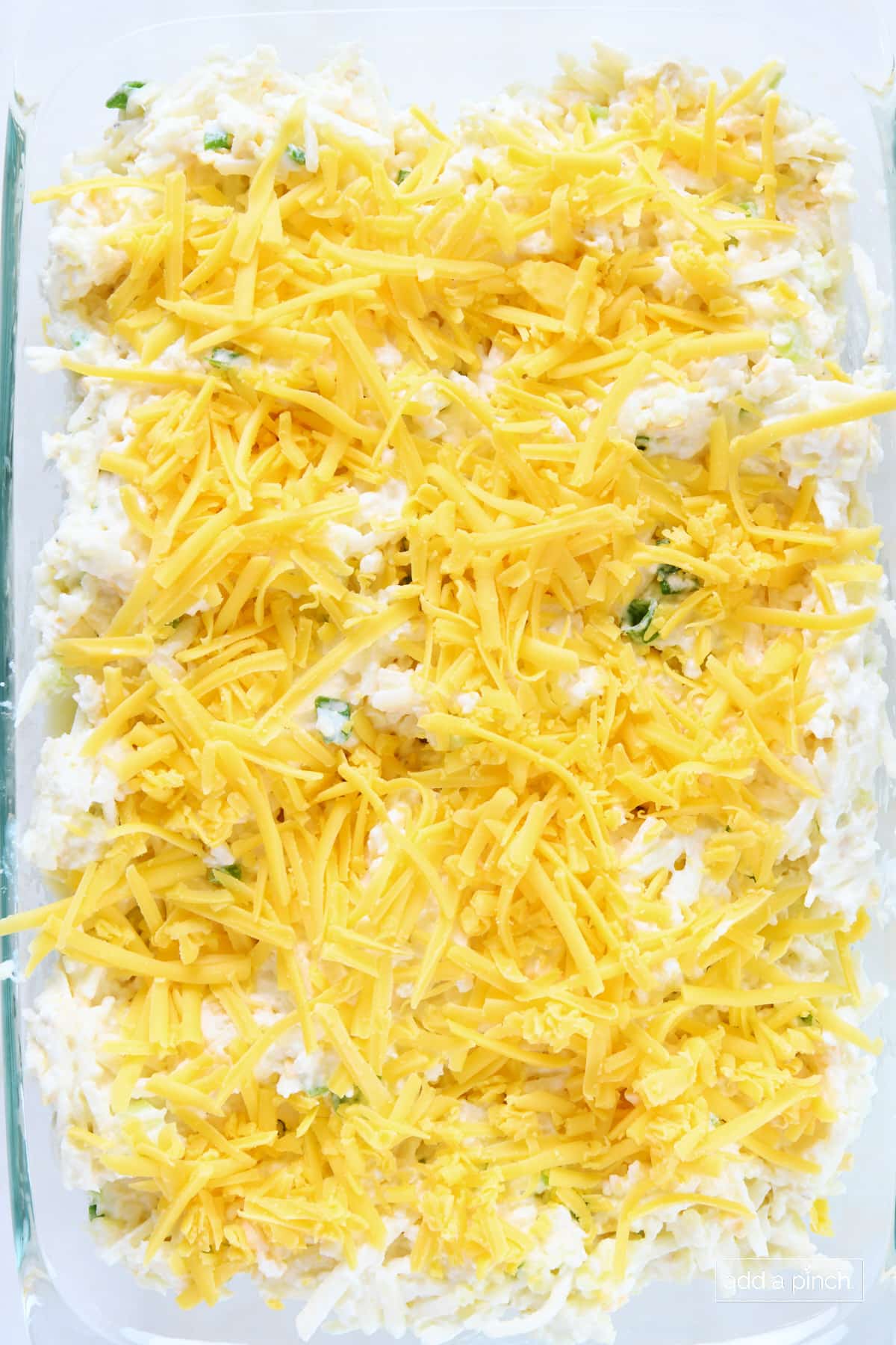 Shredded cheese topping shredded potato casserole in a glass baking dish ready to be baked.