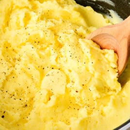 Creamy golden mashed potatoes topped with butter, salt and pepper in a white Dutch oven.
