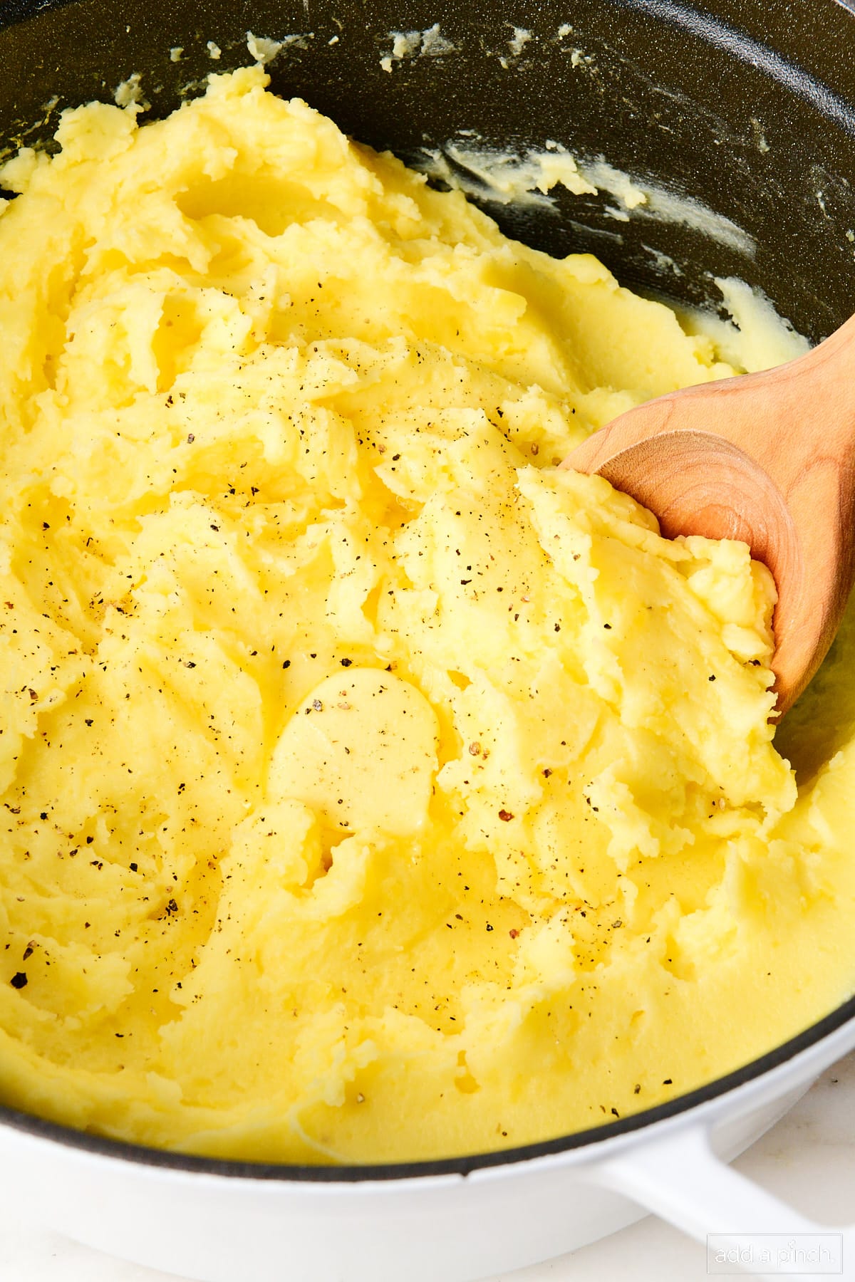 Creamy golden mashed potatoes topped with butter, salt and pepper in a white Dutch oven.