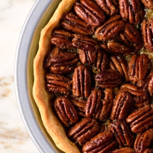 Pecan pie with golden pie crust in a pie plate on a marble counter.