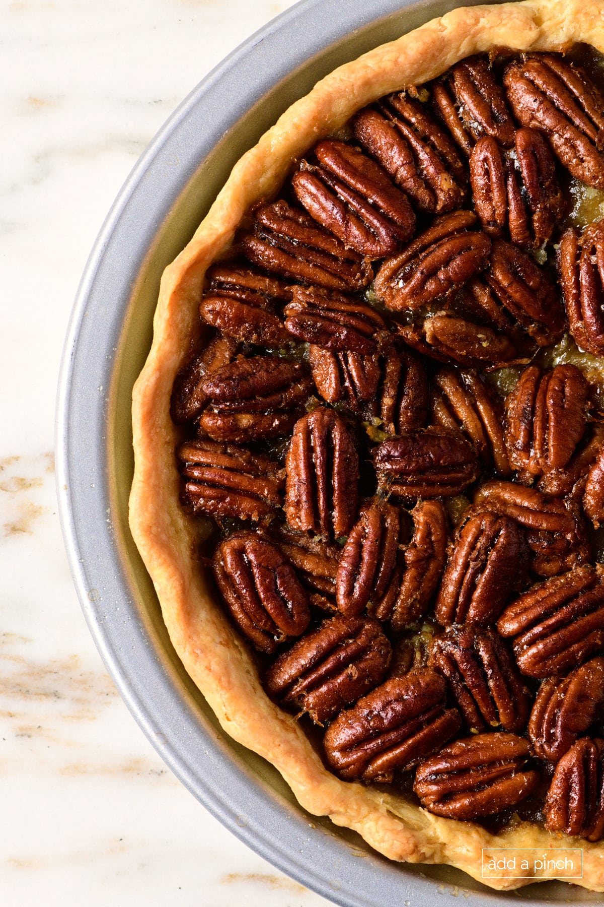 Pecan pie with golden pie crust in a pie plate on a marble counter.