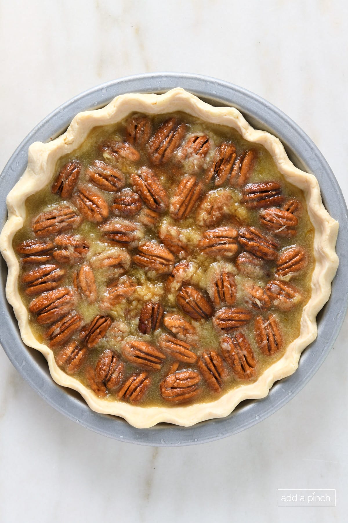 Pie plate with unbaked pie - a homemade pie crust with hand-fluted edge filled with pecan pie filling containing pecan halves. 