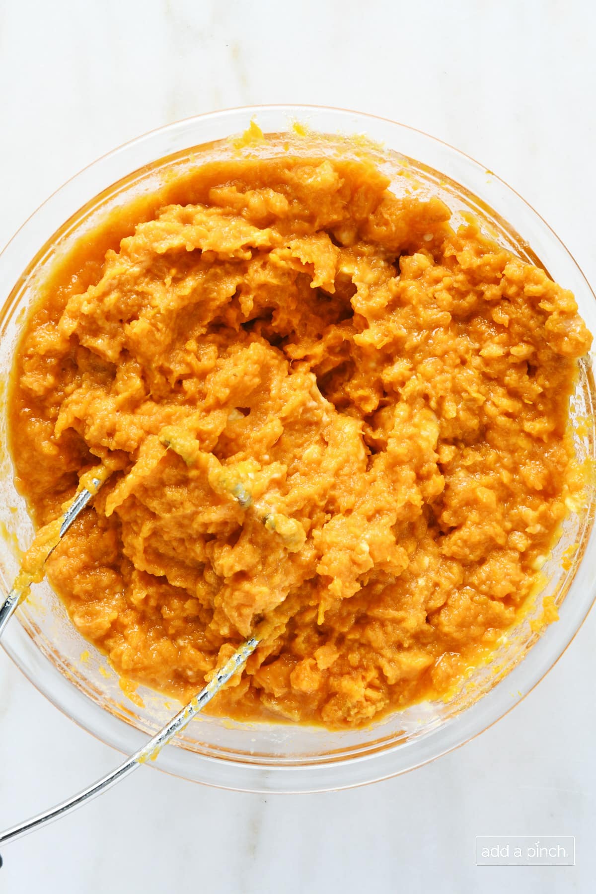 Sweet potato casserole ingredients mixed together in a glass mixing bowl.