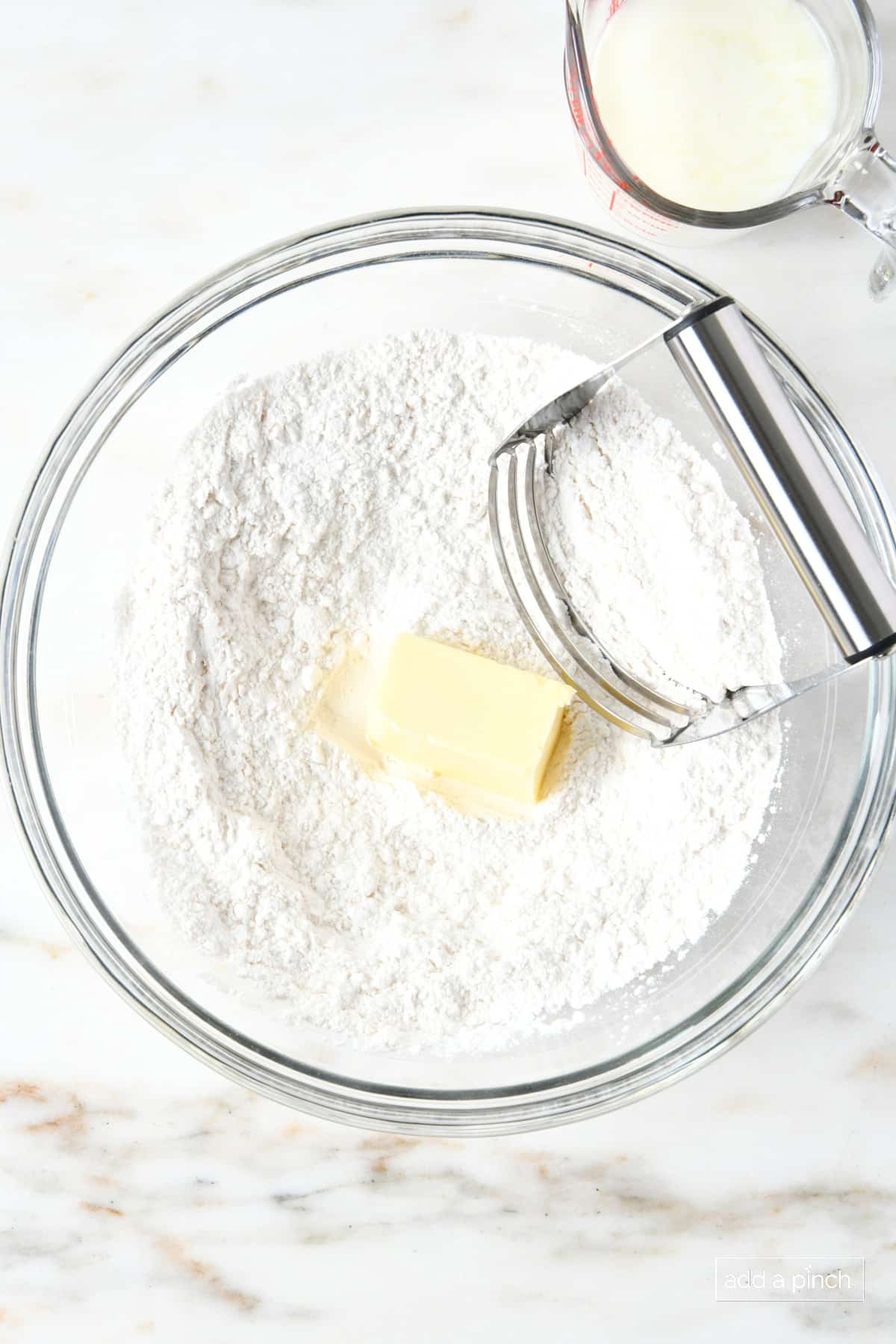Self-rising flour and butter in a glass mixing bowl with a pastry blender.