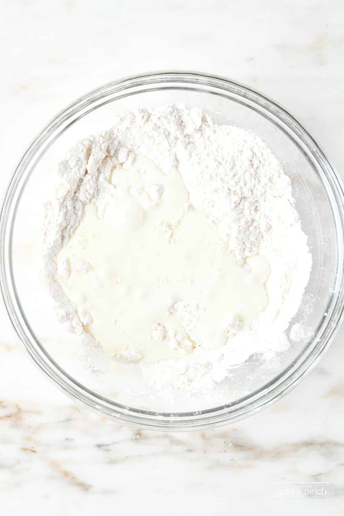 Buttermilk is added to flour in a glass bowl.