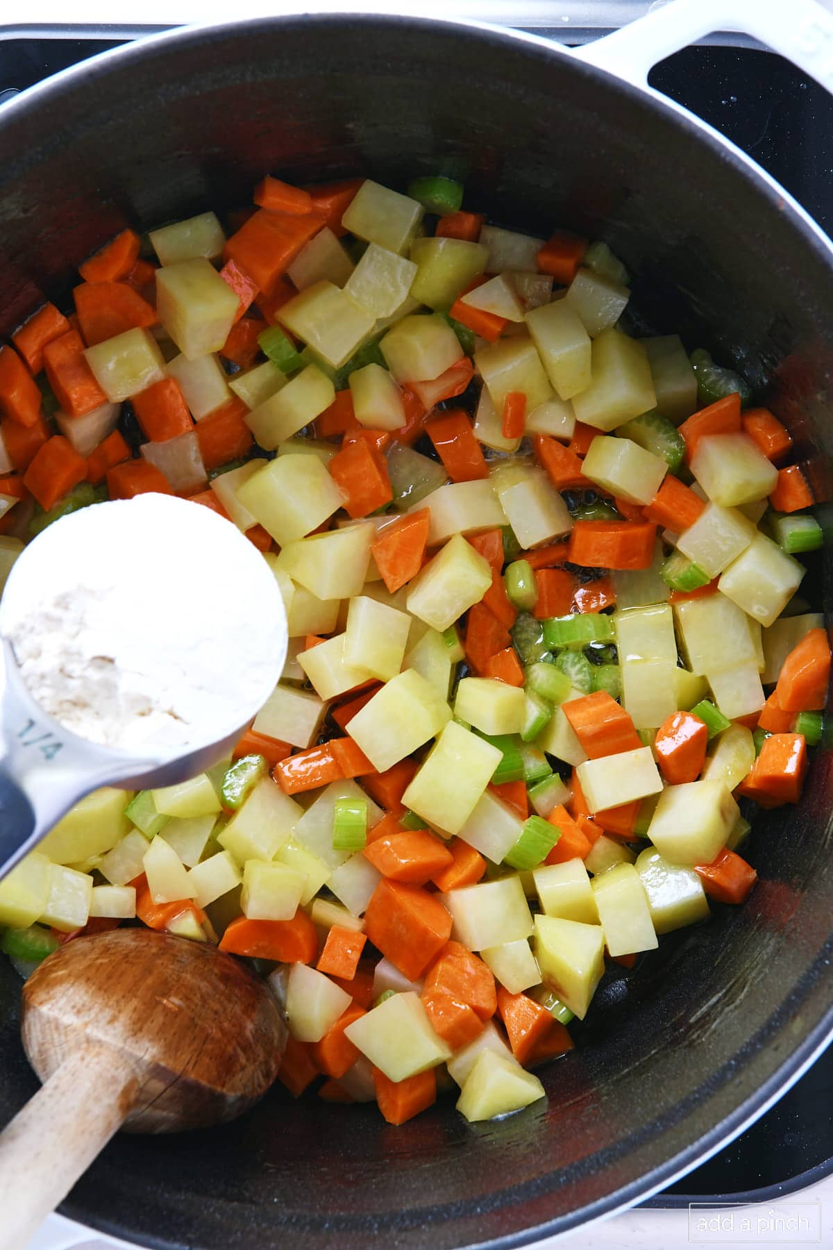 Flour adding to cooking potatoes, carrots, and celery in a dutch oven.