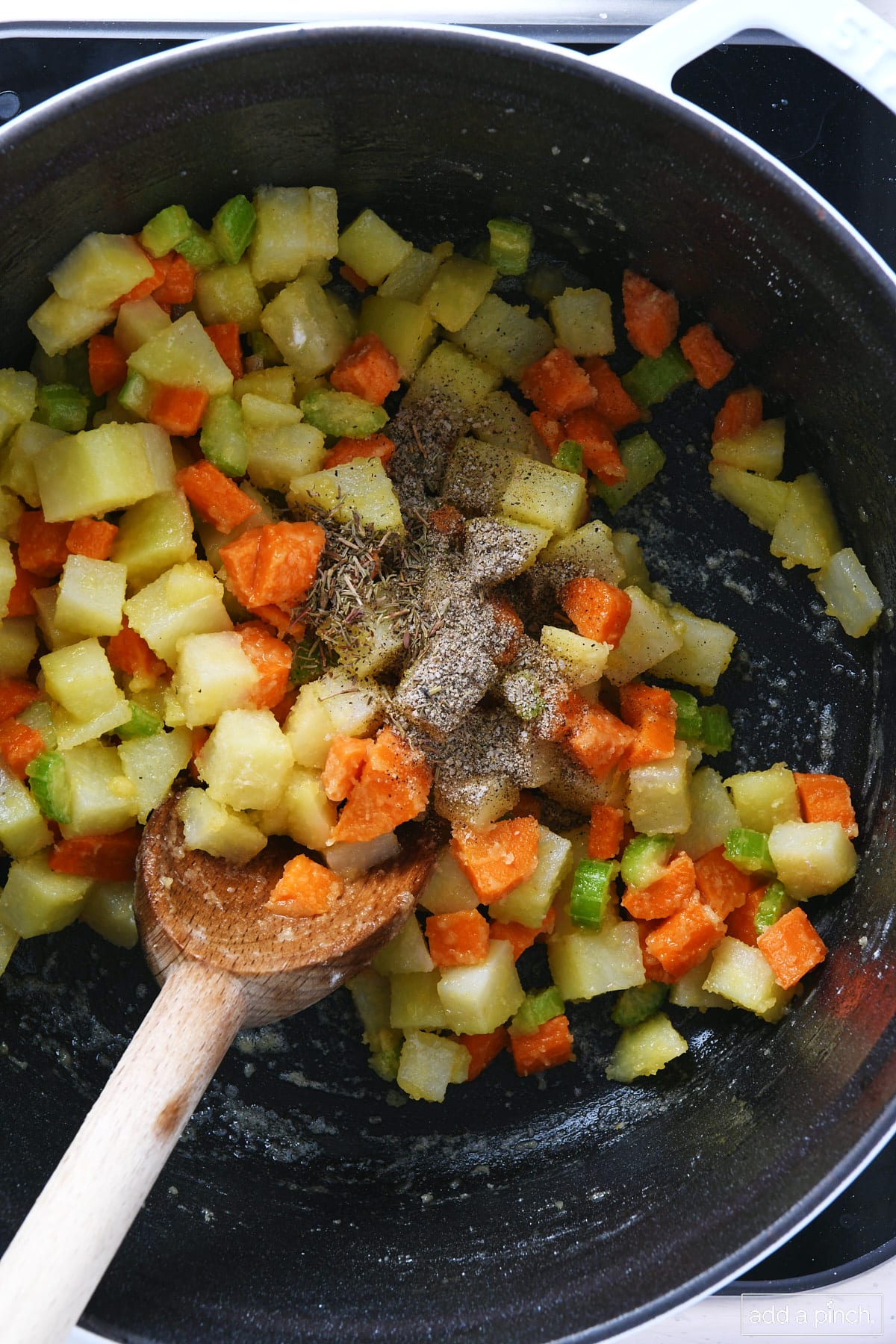 Seasonings added to potatoes, carrots, and celery in a Dutch oven.