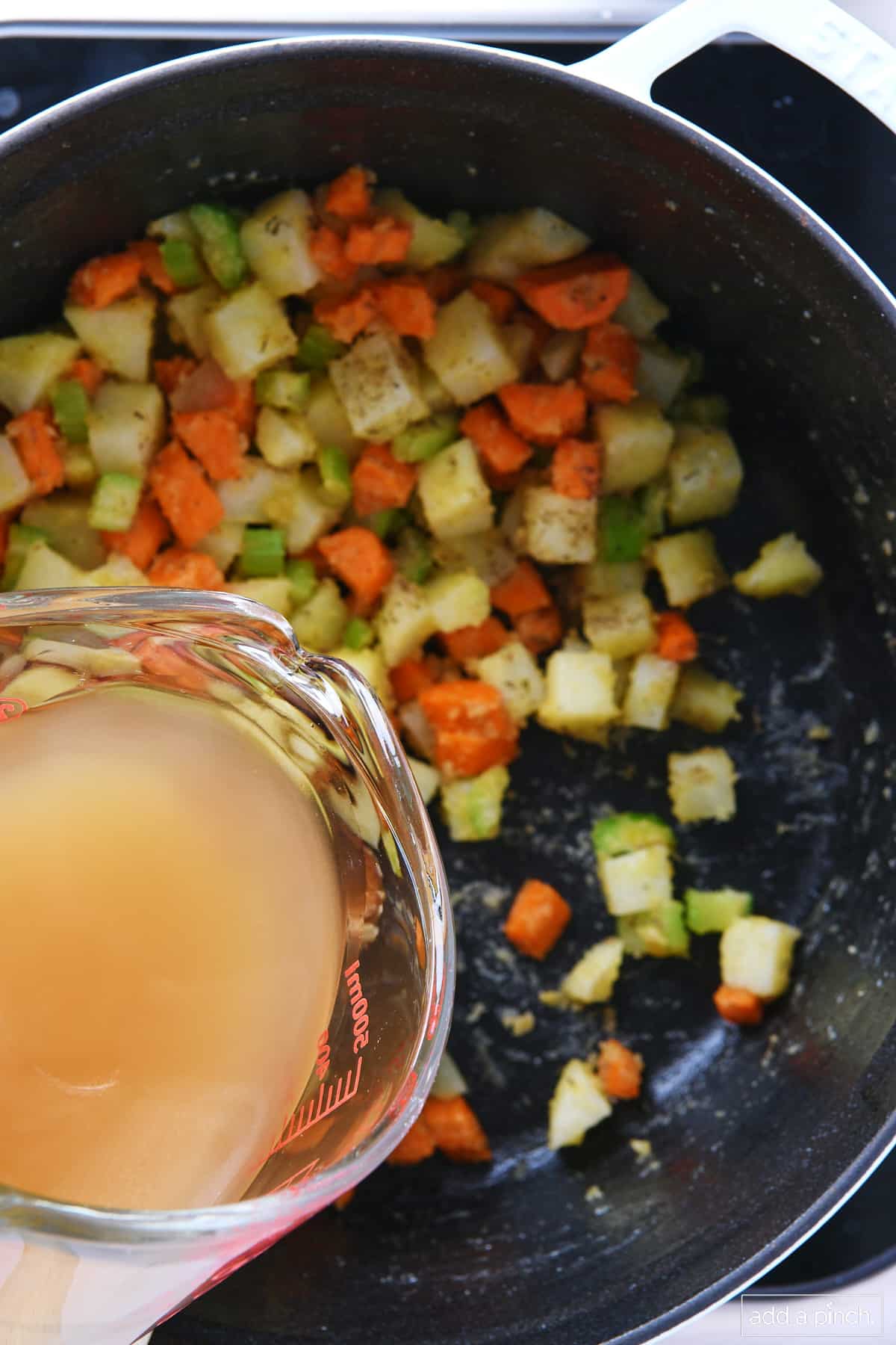 Chicken stock adding to cooked vegetables in a dutch oven.