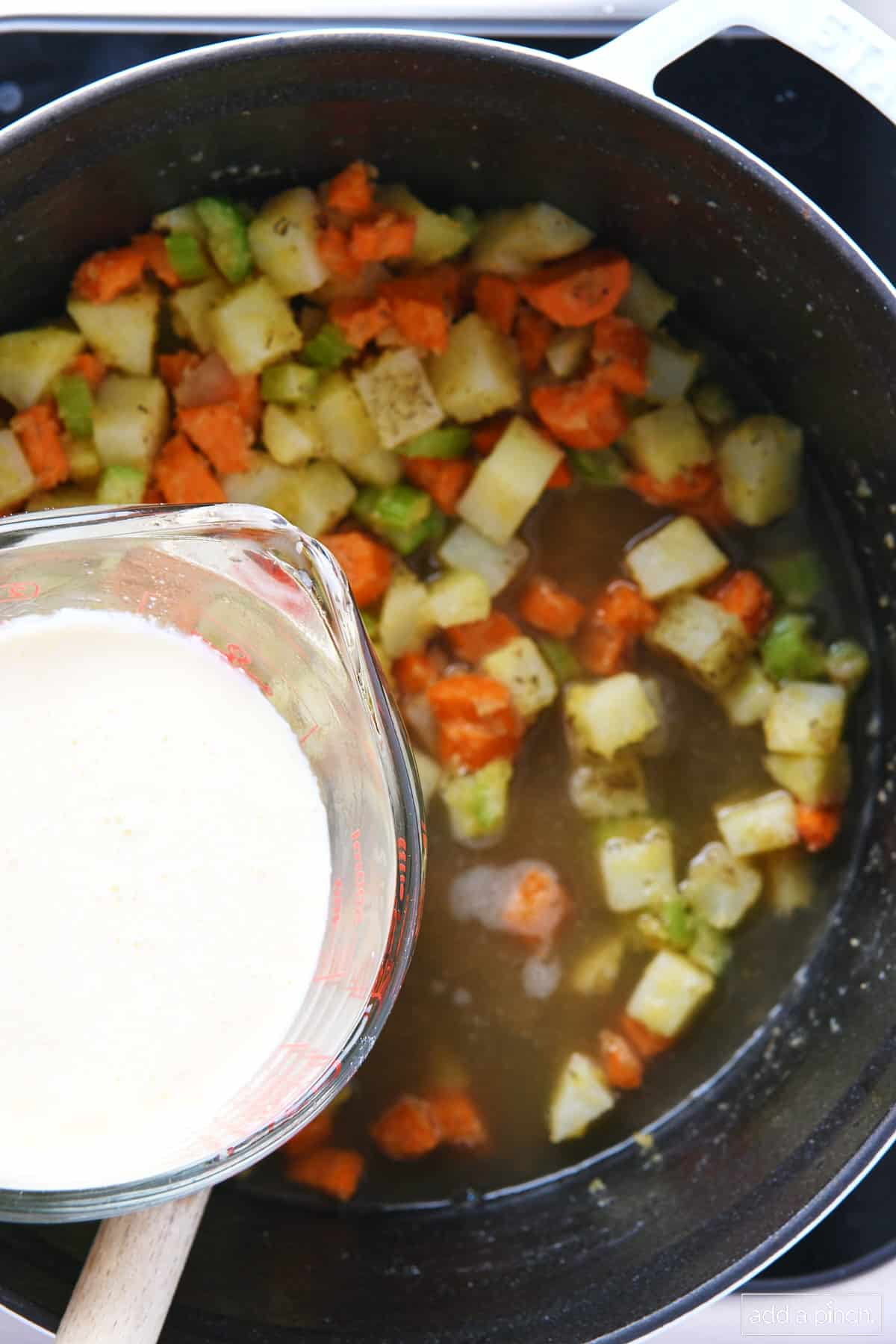 Cream being added to potatoes, carrots, and celery in a dutch oven.