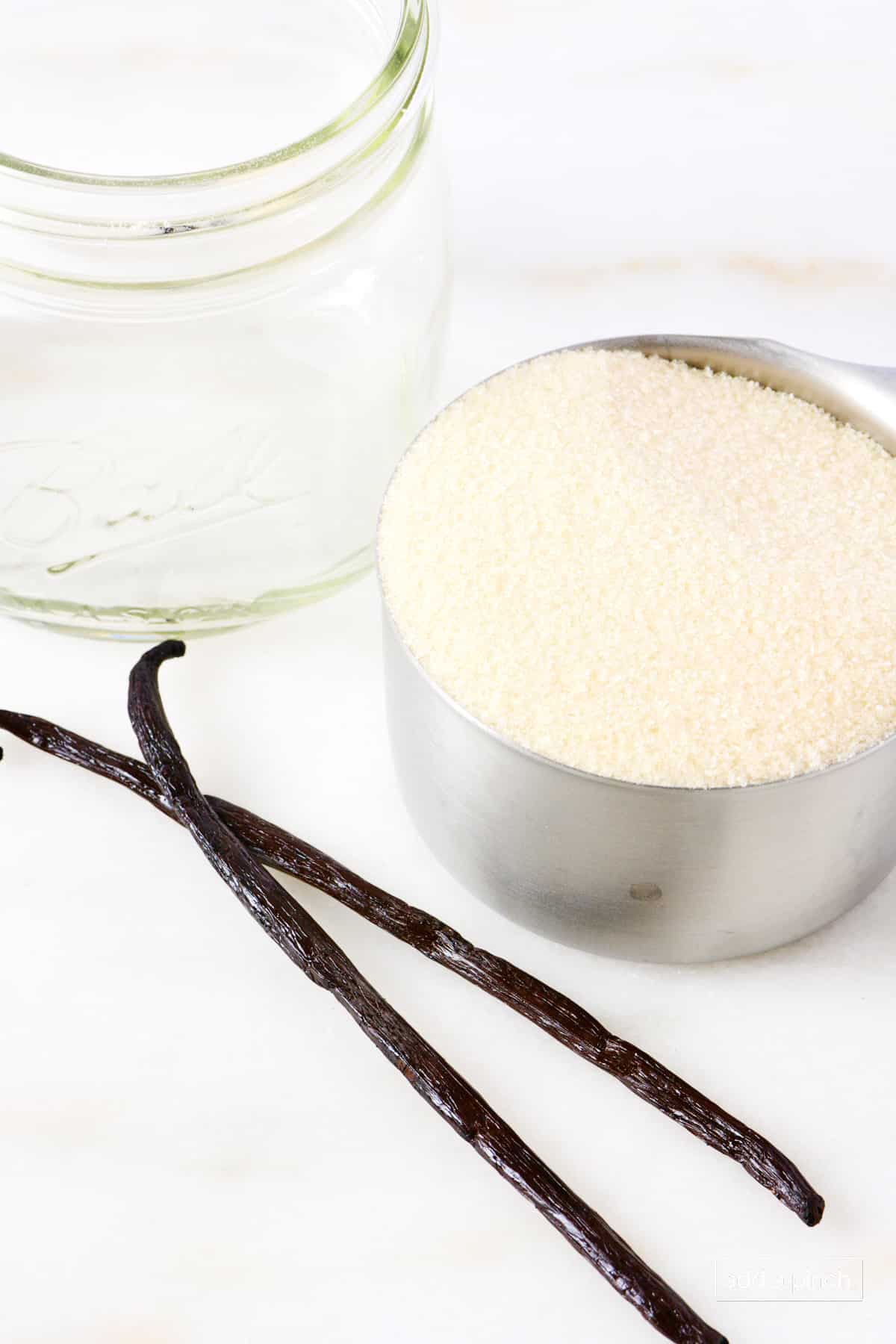 Vanilla beans, sugar, and an airtight container on a marble counter.